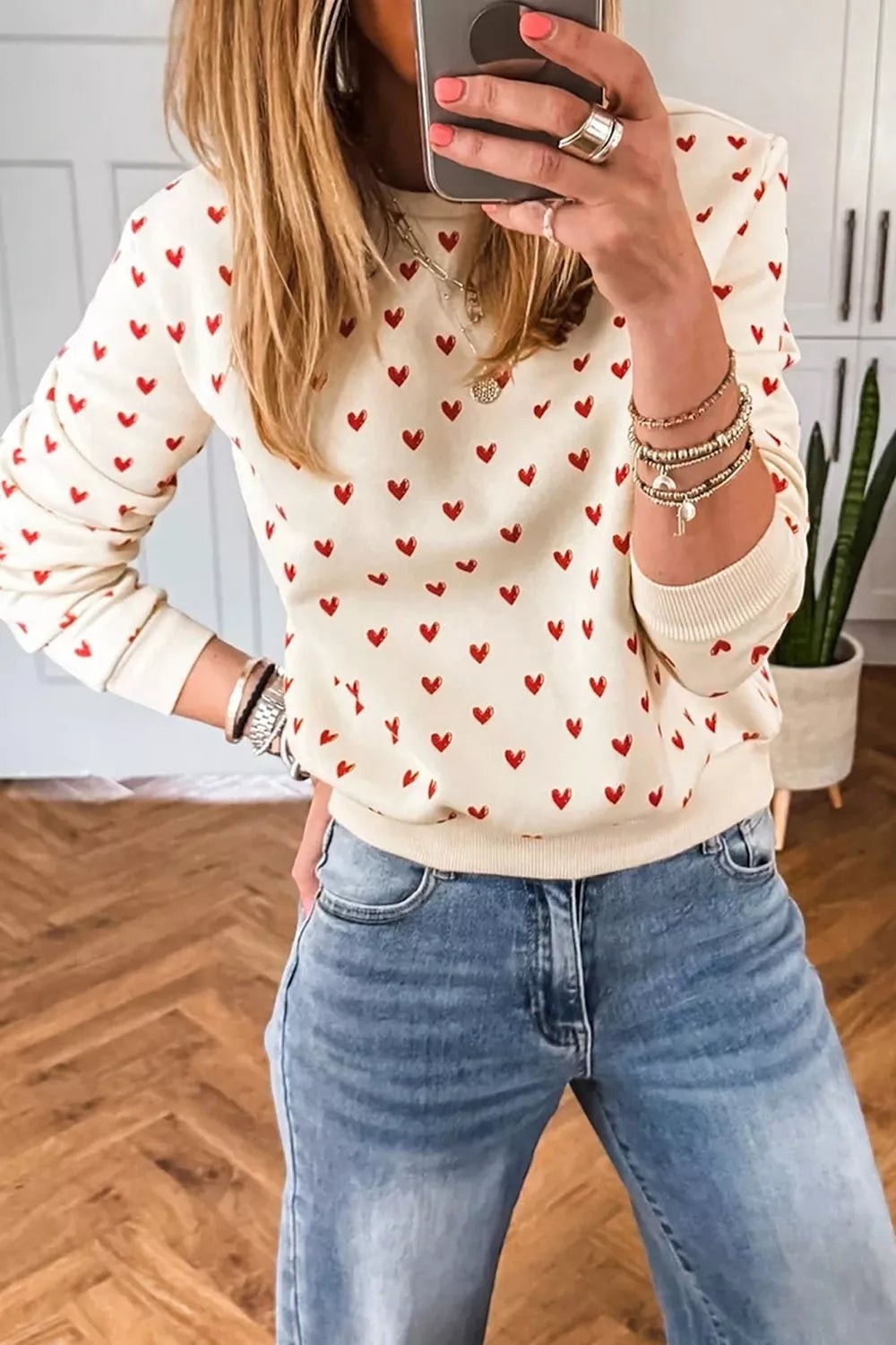 Health Hive cream long sleeve sweatshirt with small red heart print worn by a woman with blue jeans