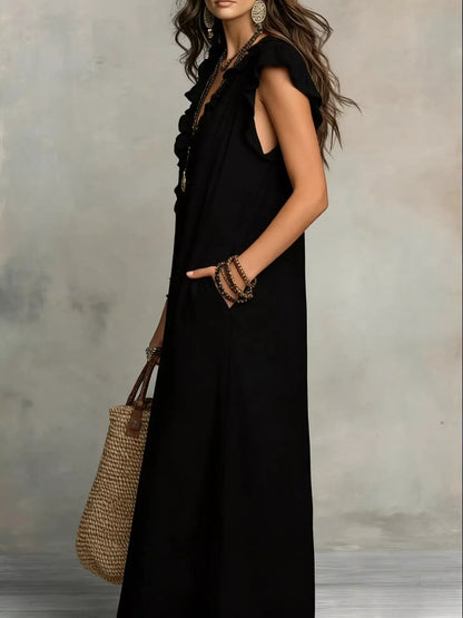 Health Hive black maxi dress with ruffled cap sleeves, V-neck, and side pockets, worn by a model with a straw bag.