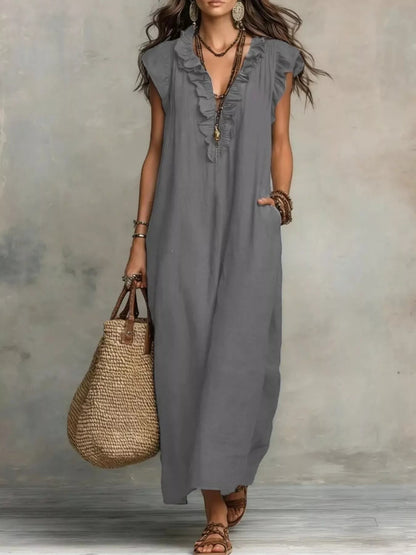 Health Hive grey ruffled V-neck maxi dress with cap sleeves and pockets, styled with a straw bag and sandals.